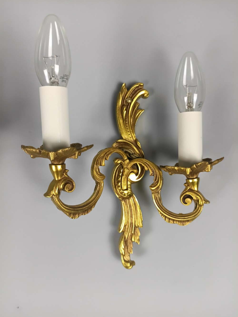 A pair of French Rococo style gilded metal twin-arm wall sconces featuring acanthus leaf scrollwork and candle-style holders. View II