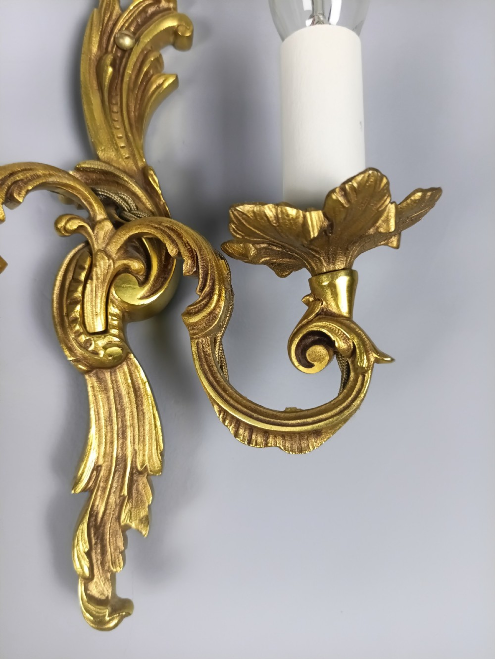 A pair of French Rococo style gilded metal twin-arm wall sconces featuring acanthus leaf scrollwork and candle-style holders. View III