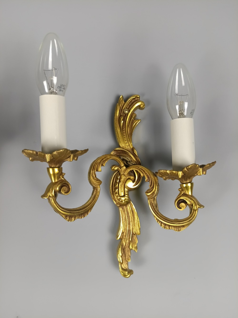 A pair of French Rococo style gilded metal twin-arm wall sconces featuring acanthus leaf scrollwork and candle-style holders. View IV