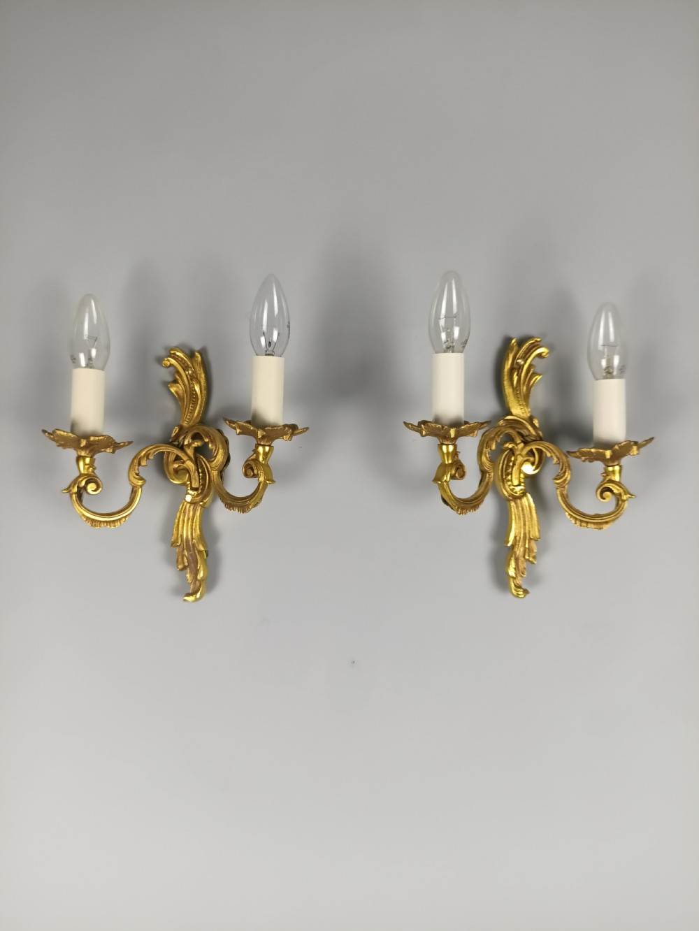 A pair of French Rococo style gilded metal twin-arm wall sconces featuring acanthus leaf scrollwork and candle-style holders. View VI
