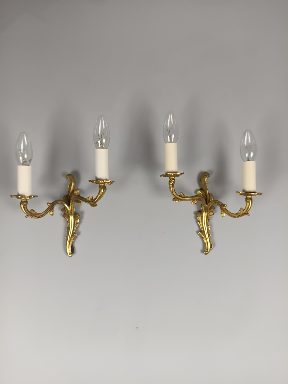 A pair of French gilt brass two-arm wall sconces featuring acanthus leaf scrollwork and candle-style bulb holders.