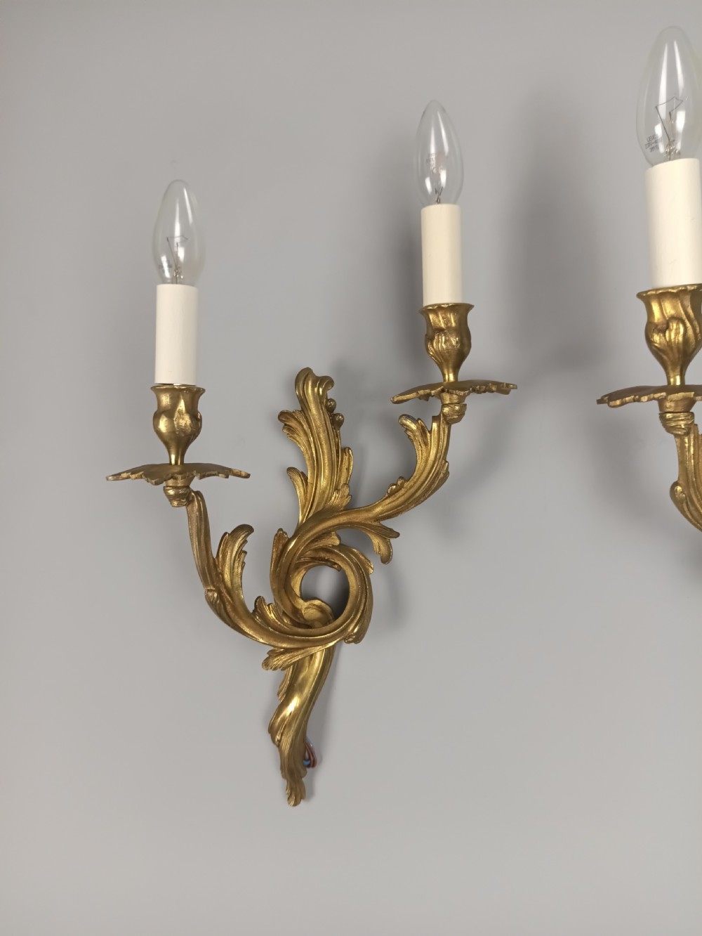 A pair of French Rococo style gilded bronze wall sconces with twin scrolling acanthus arms and candle sleeves. View V