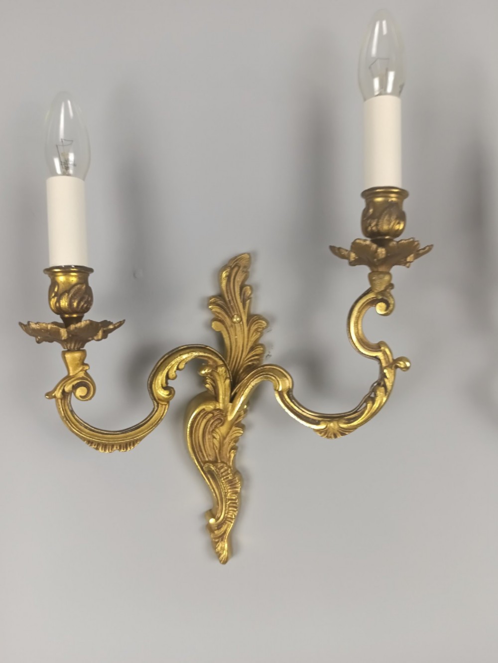 A pair of antique French Rococo gilded bronze twin-arm wall sconces featuring ornate acanthus leaf scrolling and candle sockets. View II