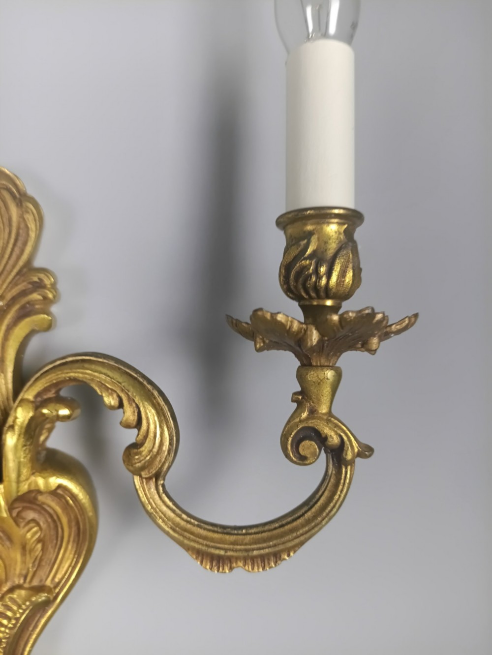 A pair of antique French Rococo gilded bronze twin-arm wall sconces featuring ornate acanthus leaf scrolling and candle sockets. View III