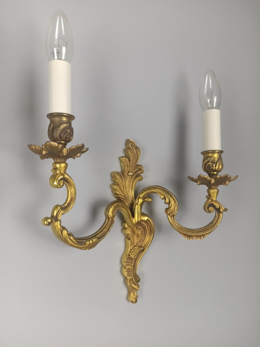 A pair of antique French Rococo gilded bronze twin-arm wall sconces featuring ornate acanthus leaf scrolling and candle sockets. View VI