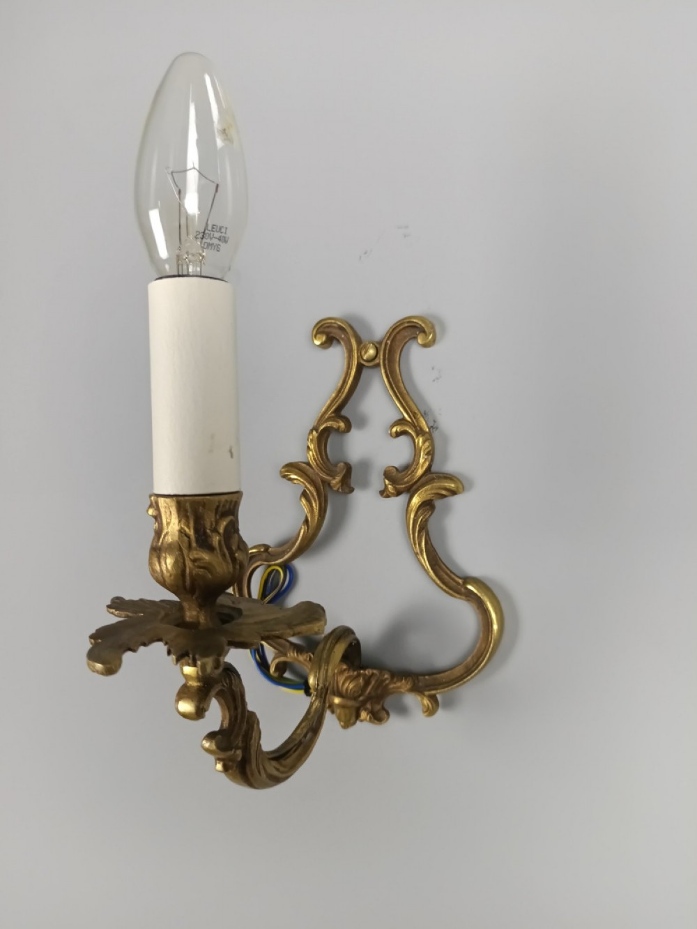 A pair of French Rococo style gilt bronze single-arm wall sconces featuring ornate scrollwork backplates and candle-style sockets. View II