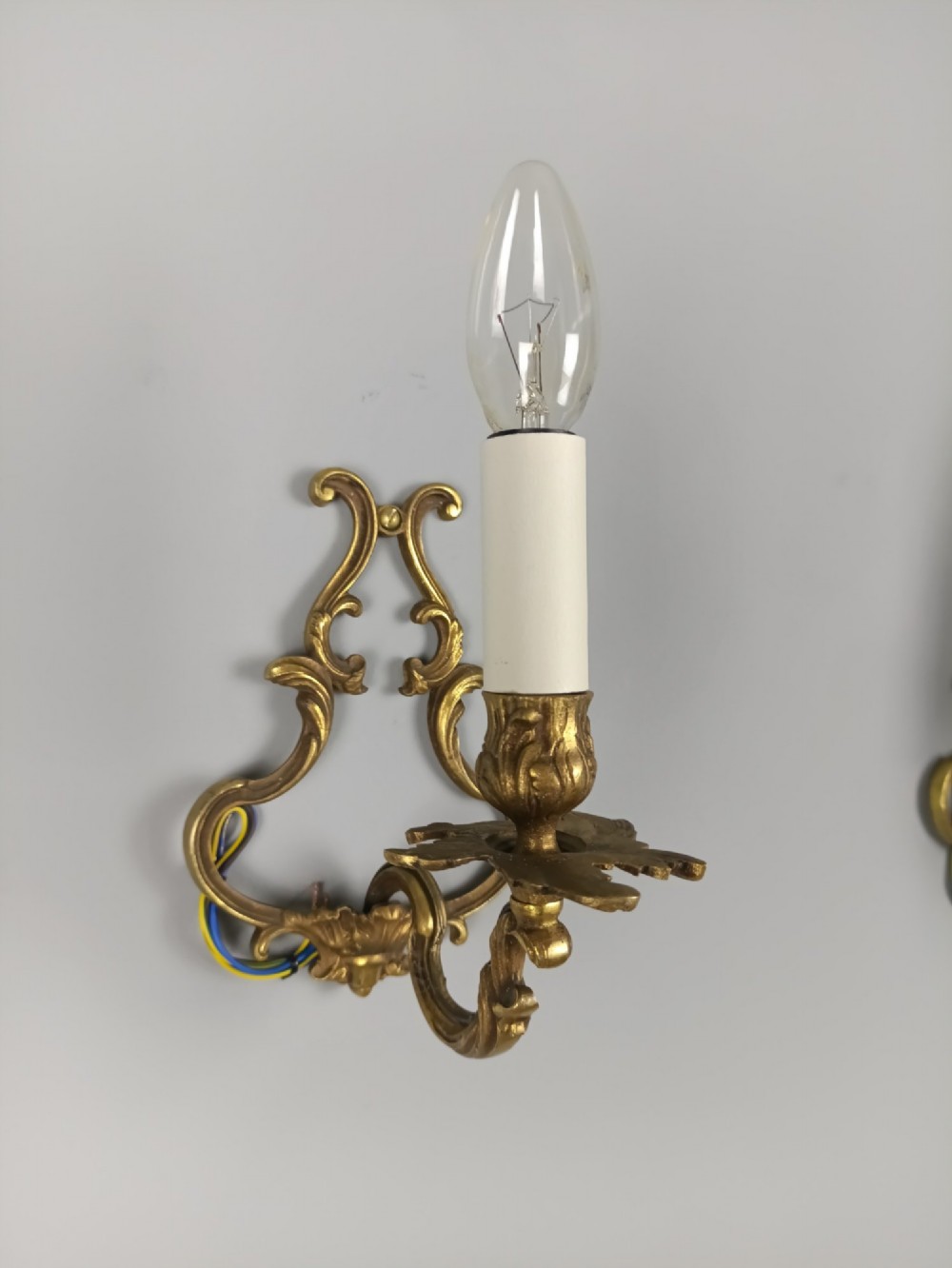 A pair of French Rococo style gilt bronze single-arm wall sconces featuring ornate scrollwork backplates and candle-style sockets. View III