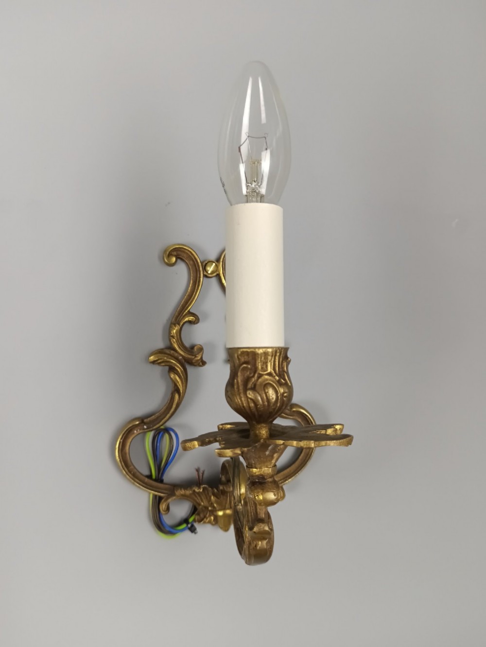 A pair of French Rococo style gilt bronze single-arm wall sconces featuring ornate scrollwork backplates and candle-style sockets. View IV