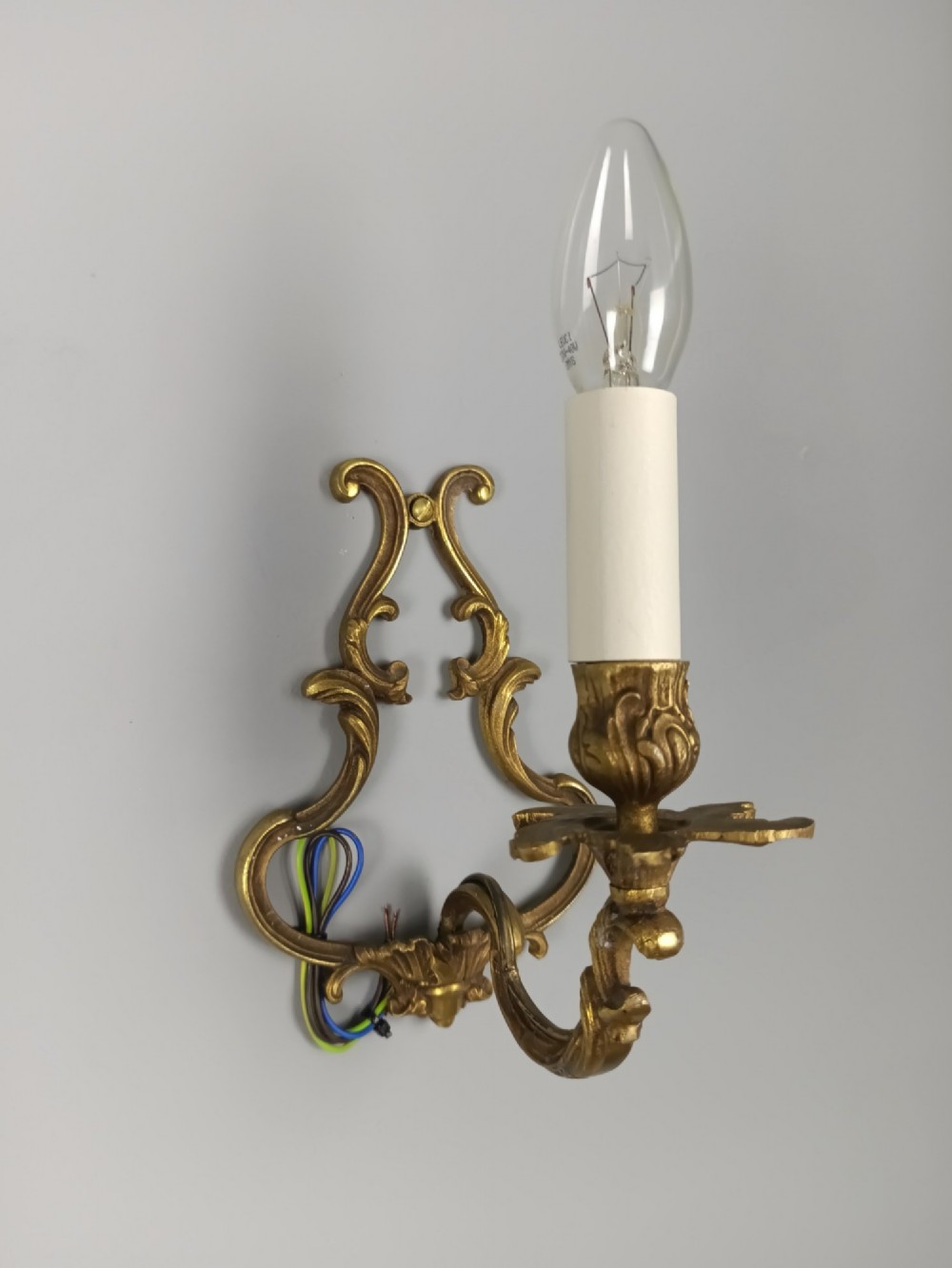 A pair of French Rococo style gilt bronze single-arm wall sconces featuring ornate scrollwork backplates and candle-style sockets. View V