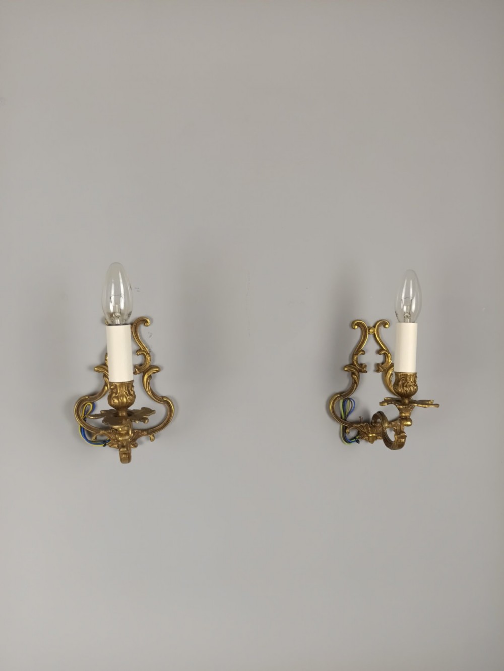A pair of French Rococo style gilt bronze single-arm wall sconces featuring ornate scrollwork backplates and candle-style sockets. View VI