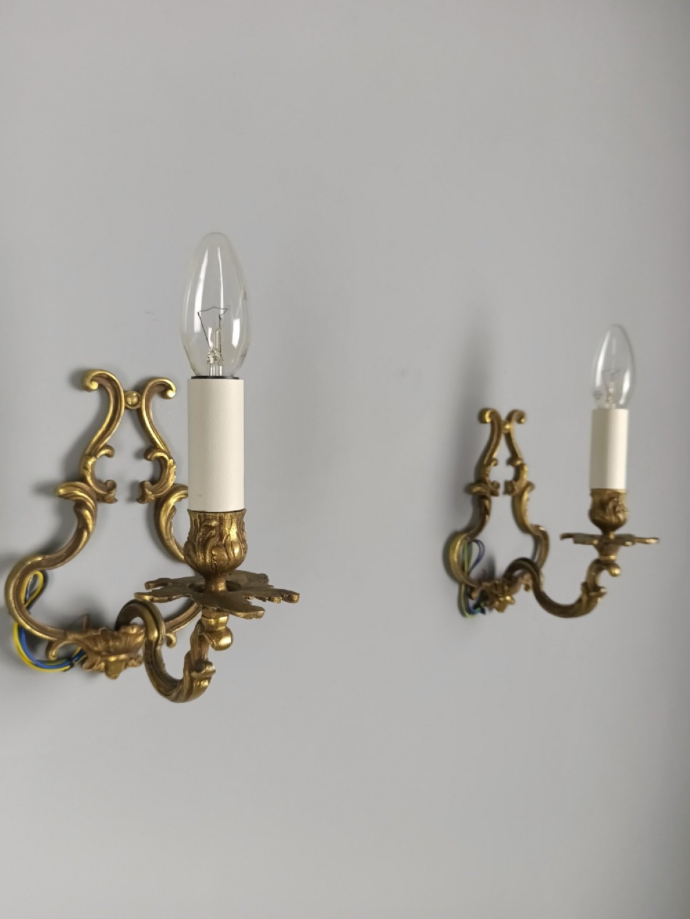 A pair of French Rococo style gilt bronze single-arm wall sconces featuring ornate scrollwork backplates and candle-style sockets.