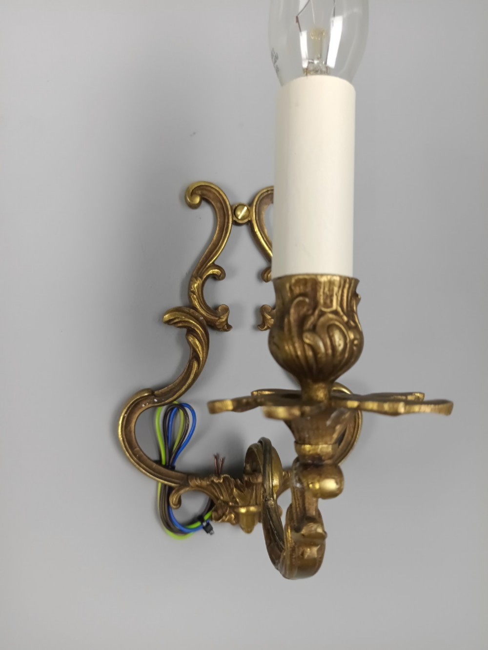 A pair of French Rococo style gilt bronze single-arm wall sconces featuring ornate scrollwork backplates and candle-style sockets. View VII