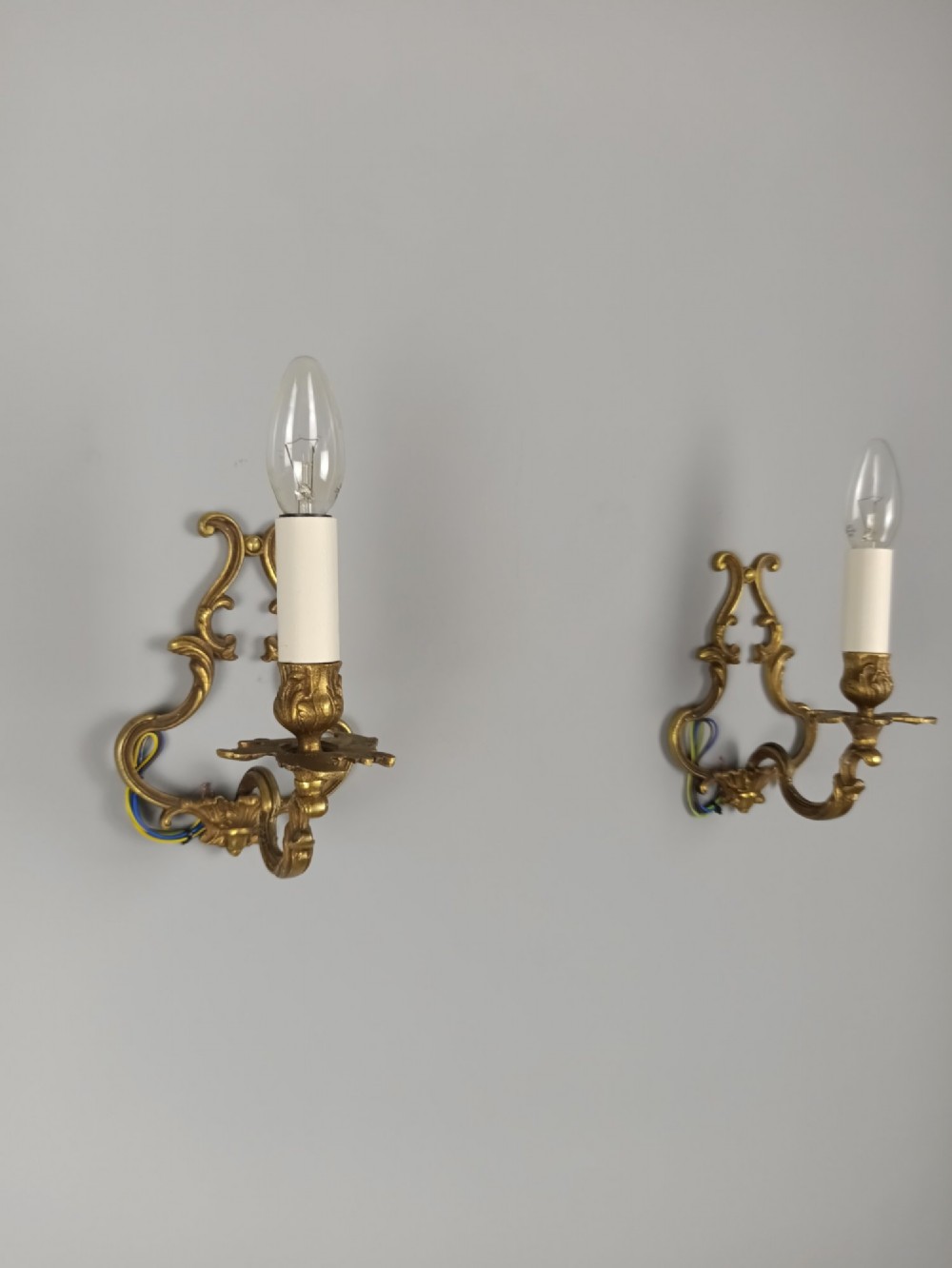 A pair of French Rococo style gilt bronze single-arm wall sconces featuring ornate scrollwork backplates and candle-style sockets. View VIII
