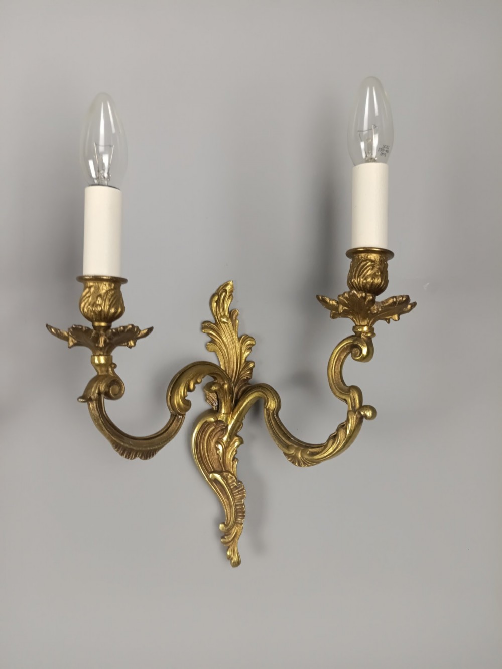 A pair of antique French Rococo gilded bronze twin-arm wall sconces featuring acanthus leaf motifs and candle sleeve light fixtures. View II