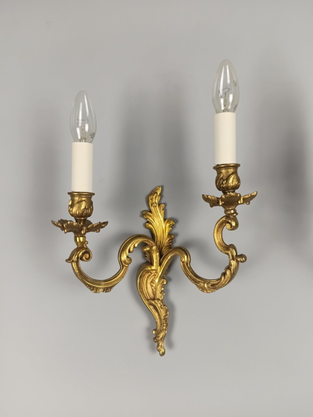 A pair of antique French Rococo gilded bronze twin-arm wall sconces featuring acanthus leaf motifs and candle sleeve light fixtures. View V