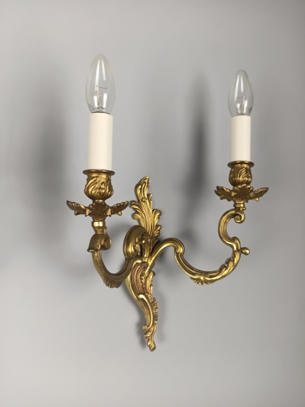 A pair of antique French Rococo gilded bronze twin-arm wall sconces featuring acanthus leaf motifs and candle sleeve light fixtures. View VI