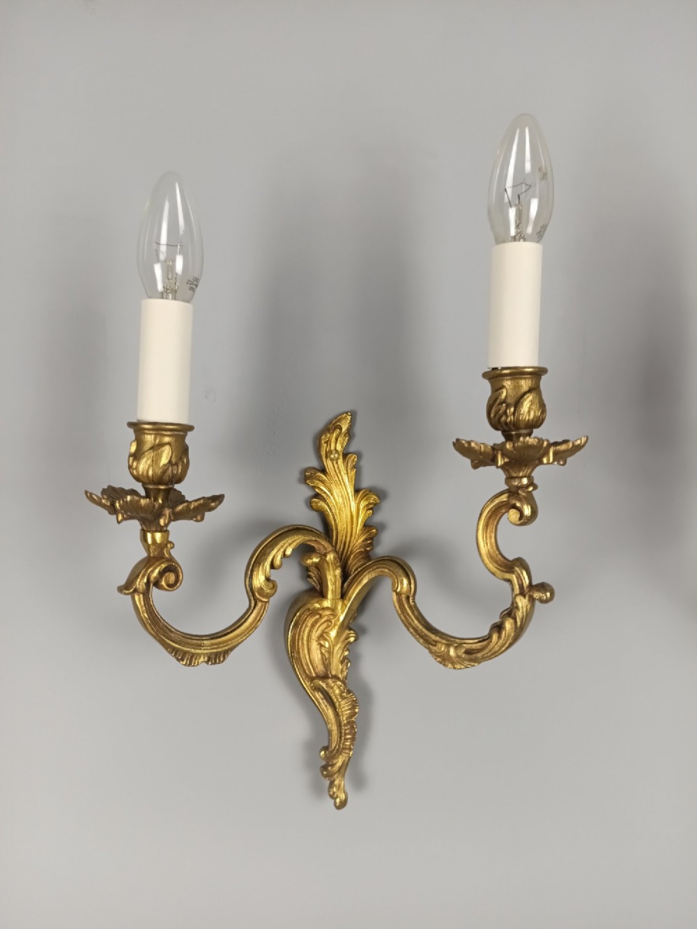A pair of antique French Rococo gilded bronze twin-arm wall sconces featuring acanthus leaf motifs and candle sleeve light fixtures. View VII