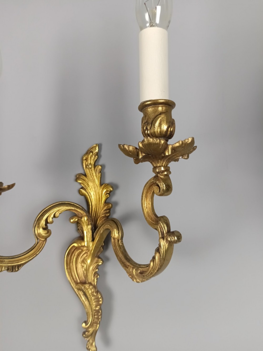 A pair of antique French Rococo gilded bronze twin-arm wall sconces featuring acanthus leaf motifs and candle sleeve light fixtures. View VIII