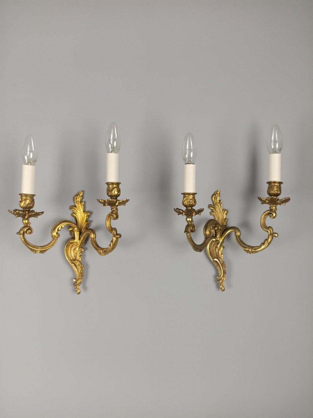 A pair of antique French Rococo gilded bronze twin-arm wall sconces featuring acanthus leaf motifs and candle sleeve light fixtures. View IX