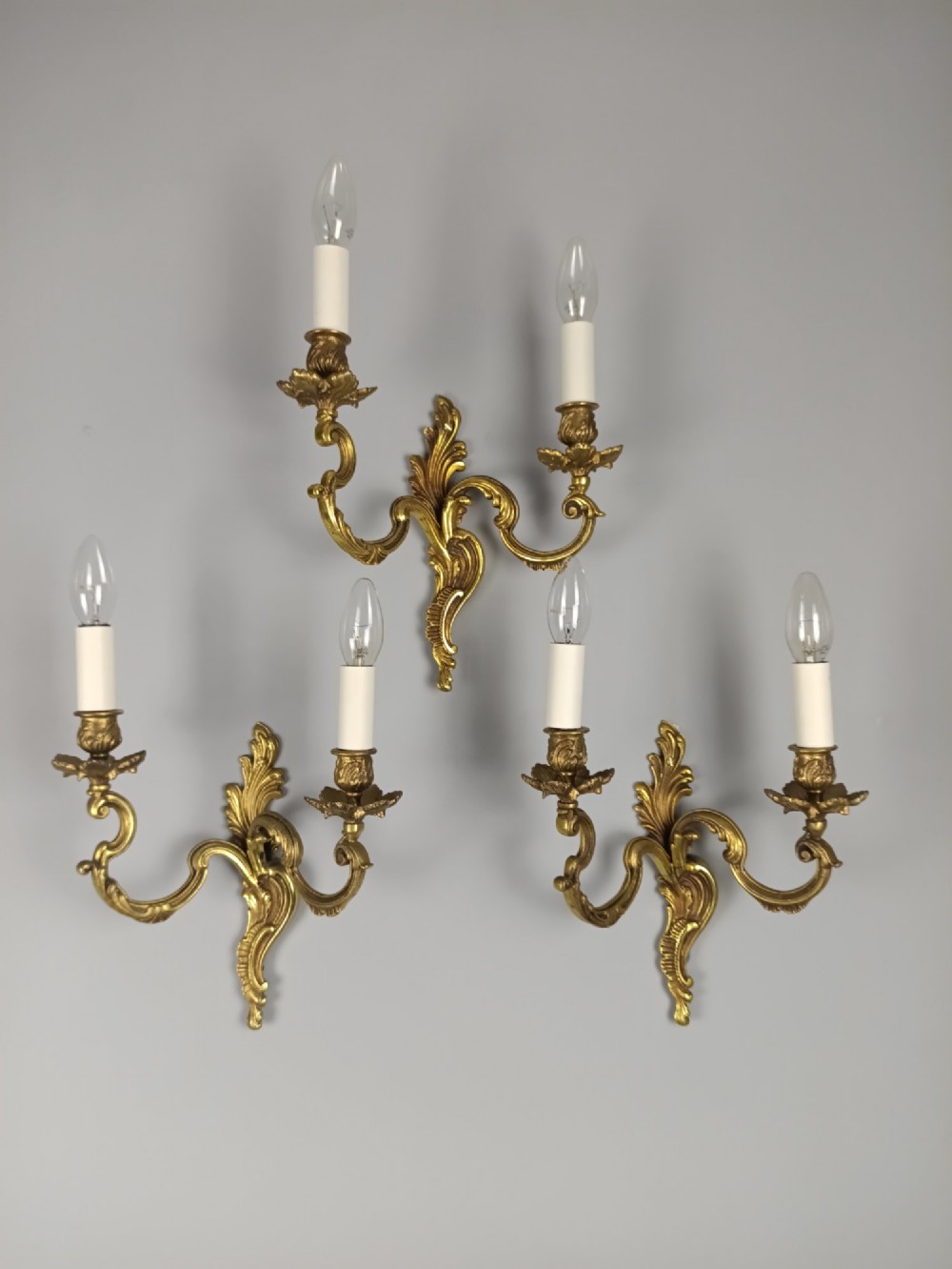 A set of three French antique gilded bronze twin-arm wall sconces featuring acanthus leaf scrolling motifs and candle sleeves.