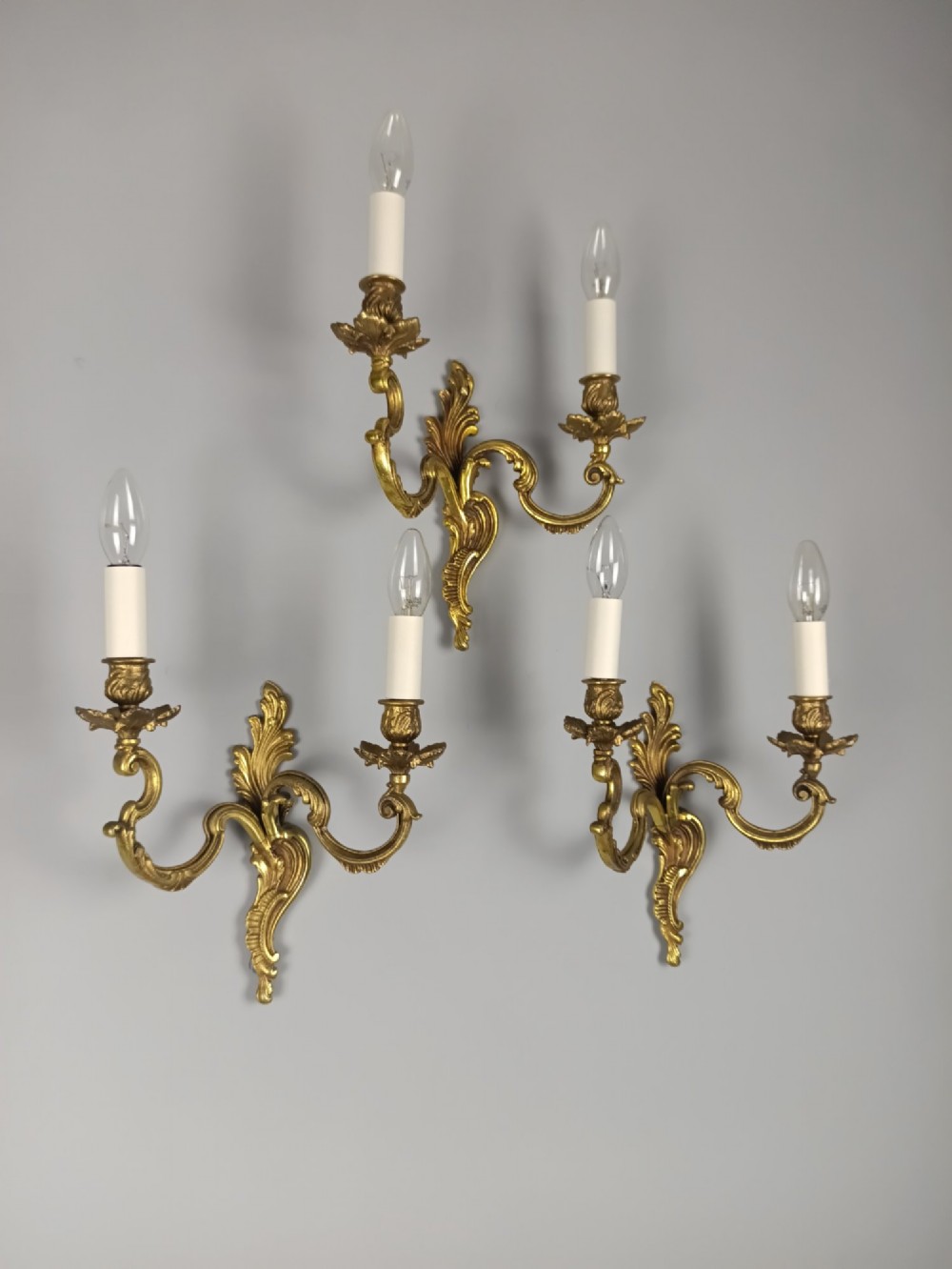 A set of three French antique gilded bronze twin-arm wall sconces featuring acanthus leaf scrolling motifs and candle sleeves. View II