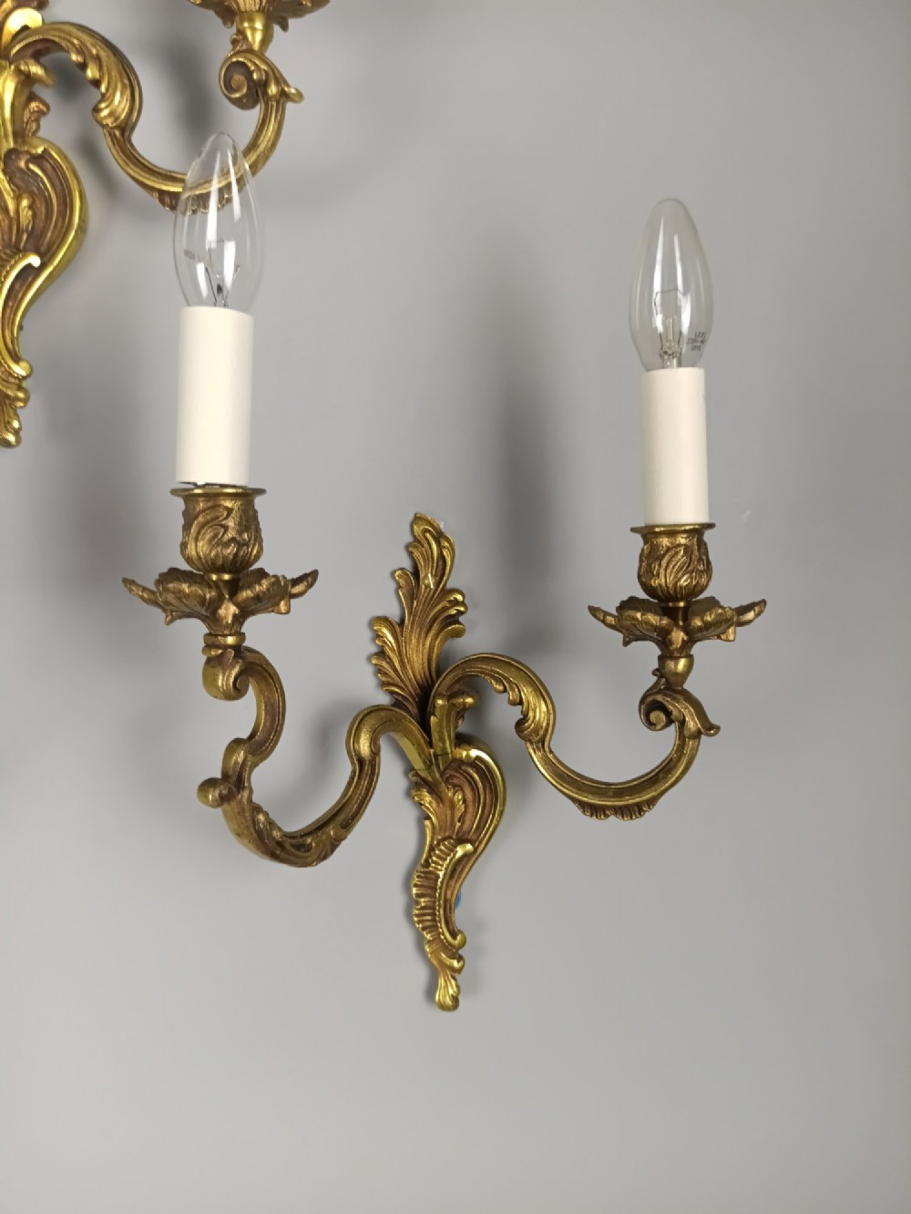 A set of three French antique gilded bronze twin-arm wall sconces featuring acanthus leaf scrolling motifs and candle sleeves. View V