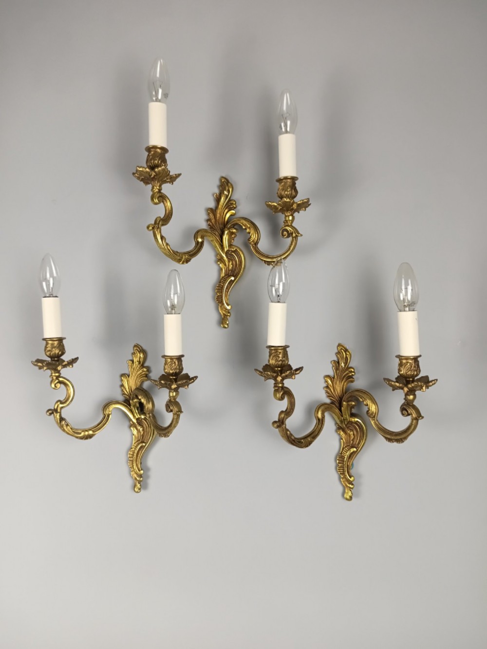 A set of three French antique gilded bronze twin-arm wall sconces featuring acanthus leaf scrolling motifs and candle sleeves. View VIII