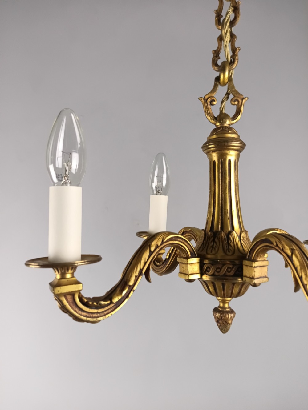 A French four-arm gilt bronze chandelier featuring acanthus leaf castings, white candle sleeves, and a suspended central chain. View II