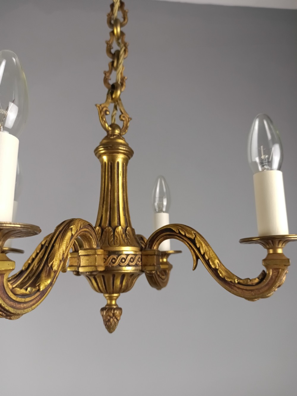 A French four-arm gilt bronze chandelier featuring acanthus leaf castings, white candle sleeves, and a suspended central chain. View III