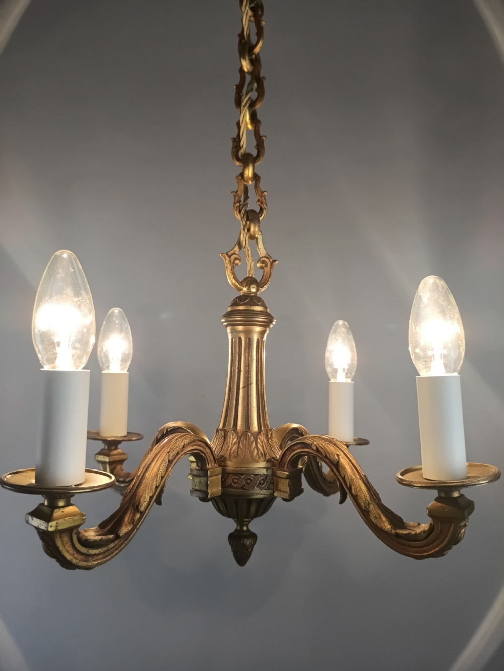 A French four-arm gilt bronze chandelier featuring acanthus leaf castings, white candle sleeves, and a suspended central chain. View IV