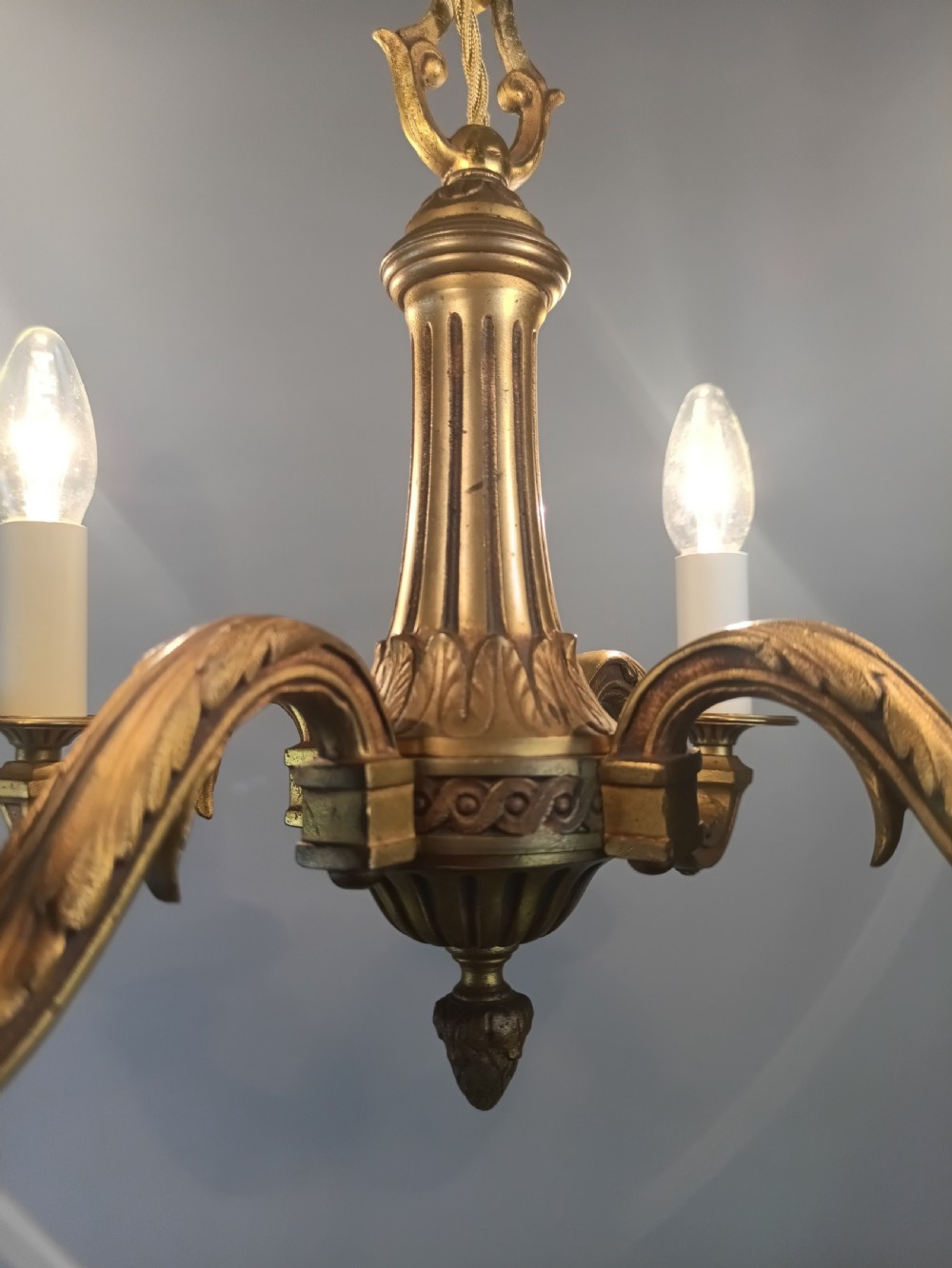 A French four-arm gilt bronze chandelier featuring acanthus leaf castings, white candle sleeves, and a suspended central chain. View V