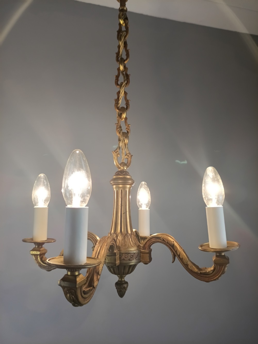 A French four-arm gilt bronze chandelier featuring acanthus leaf castings, white candle sleeves, and a suspended central chain. View VI