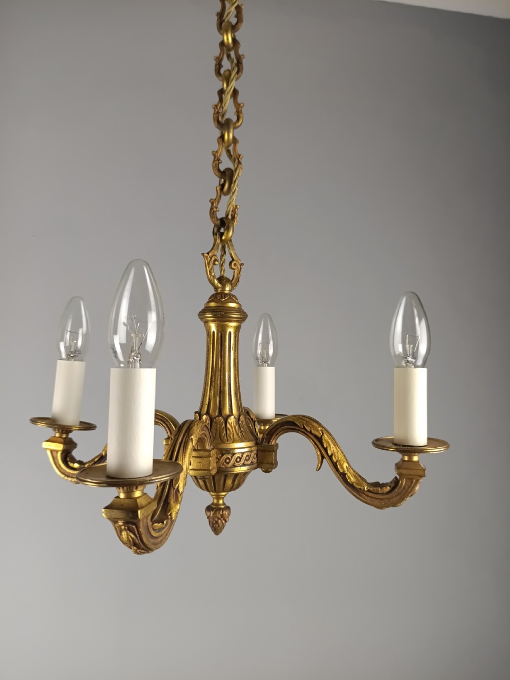A French four-arm gilt bronze chandelier featuring acanthus leaf castings, white candle sleeves, and a suspended central chain. View VII