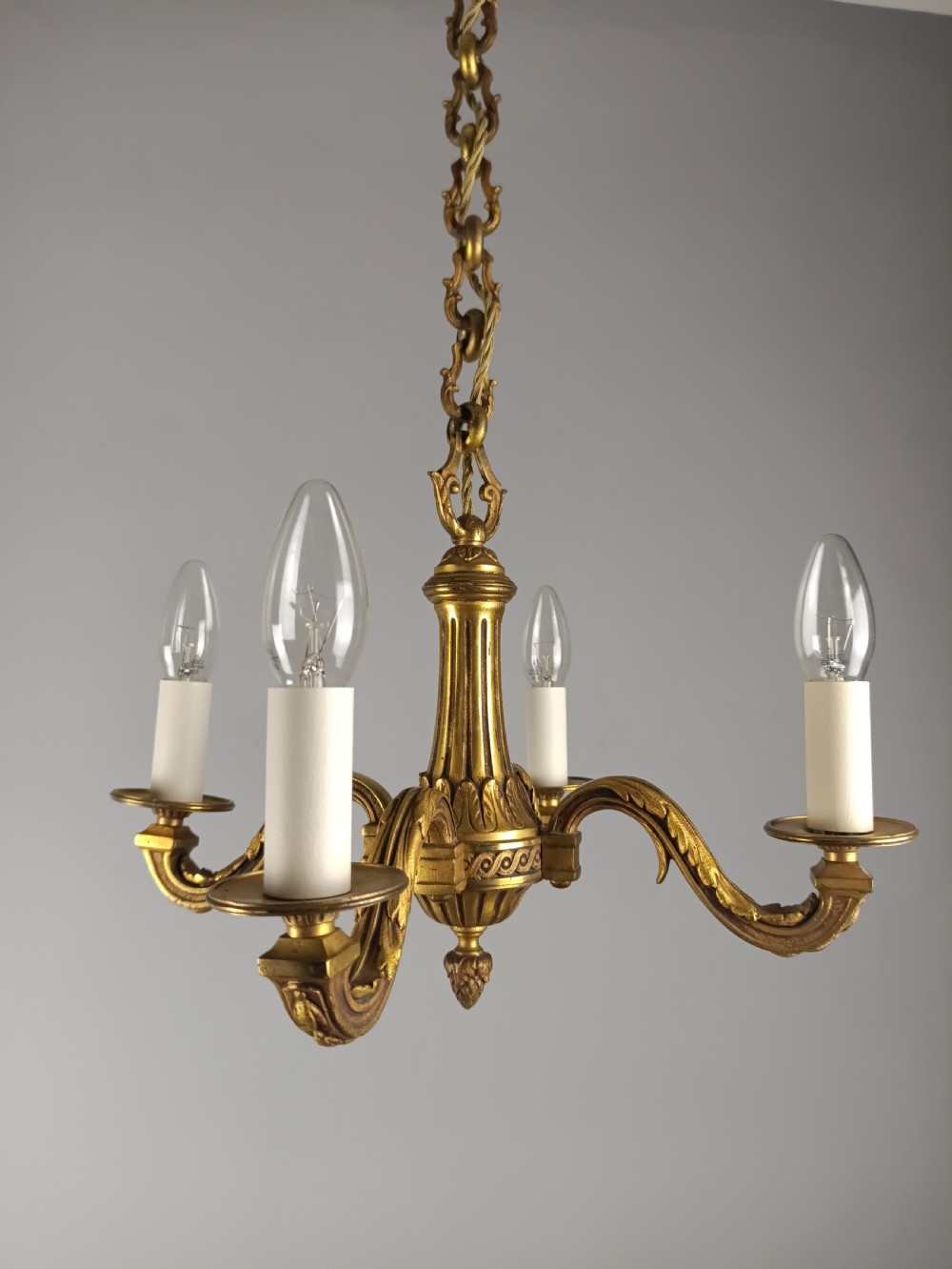 A French four-arm gilt bronze chandelier featuring acanthus leaf castings, white candle sleeves, and a suspended central chain. View VIII