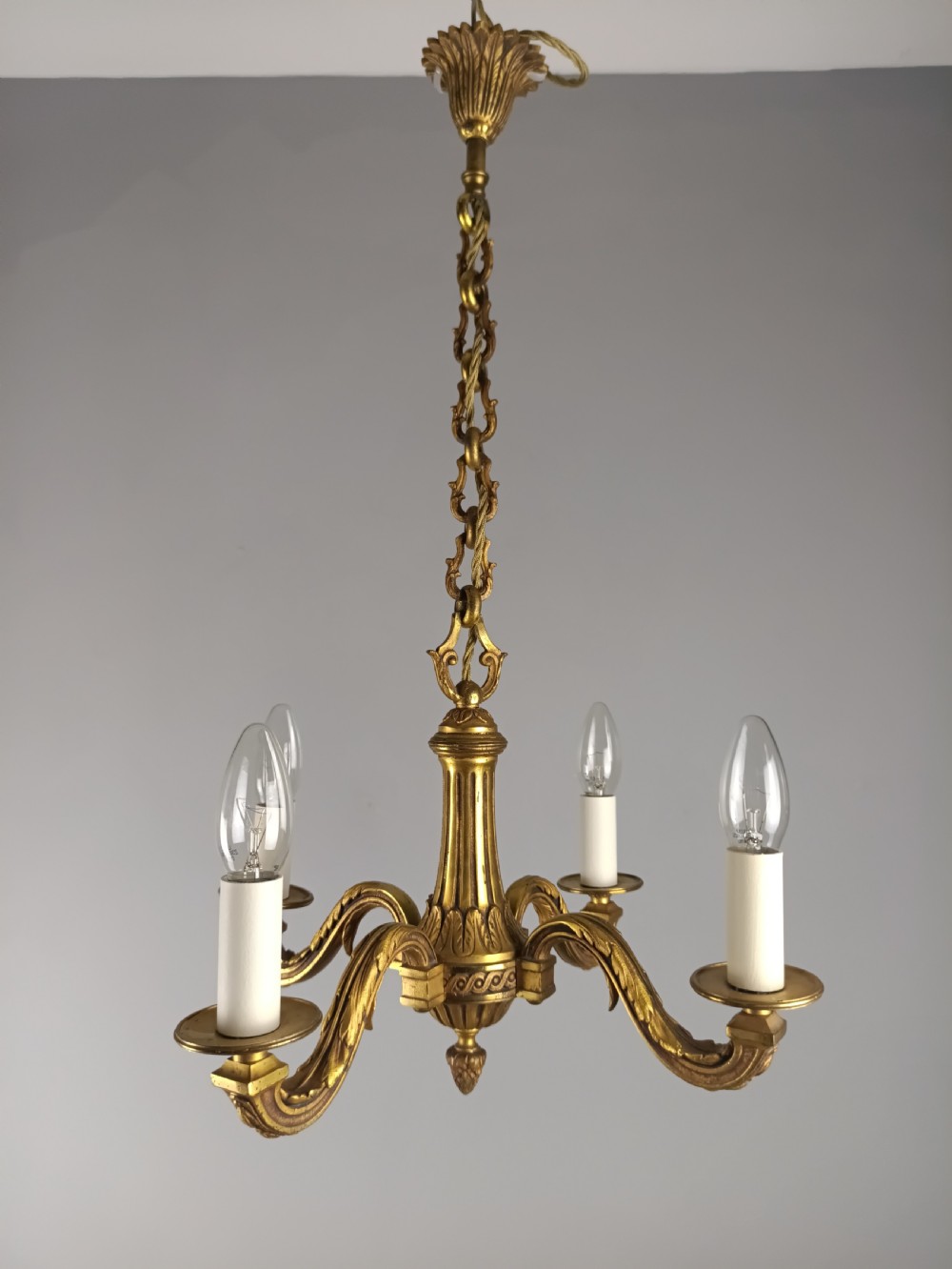 A French four-arm gilt bronze chandelier featuring acanthus leaf castings, white candle sleeves, and a suspended central chain. View IX