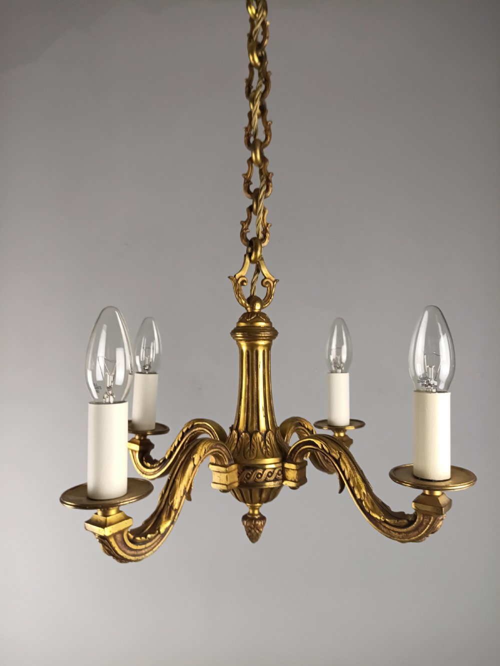 A French four-arm gilt bronze chandelier featuring acanthus leaf castings, white candle sleeves, and a suspended central chain. View X