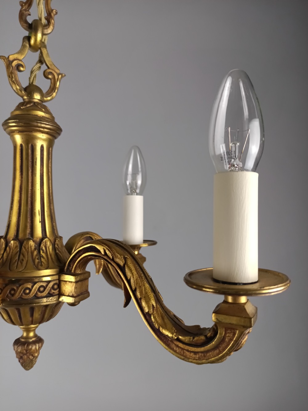 A French four-arm gilt bronze chandelier featuring acanthus leaf castings, white candle sleeves, and a suspended central chain. View XI