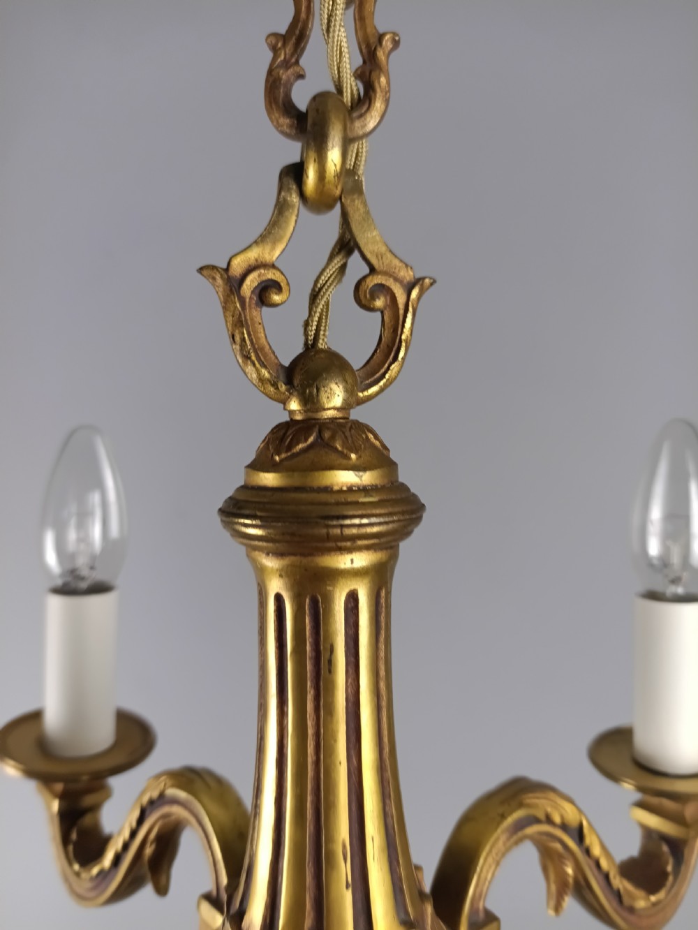 A French four-arm gilt bronze chandelier featuring acanthus leaf castings, white candle sleeves, and a suspended central chain. View XII