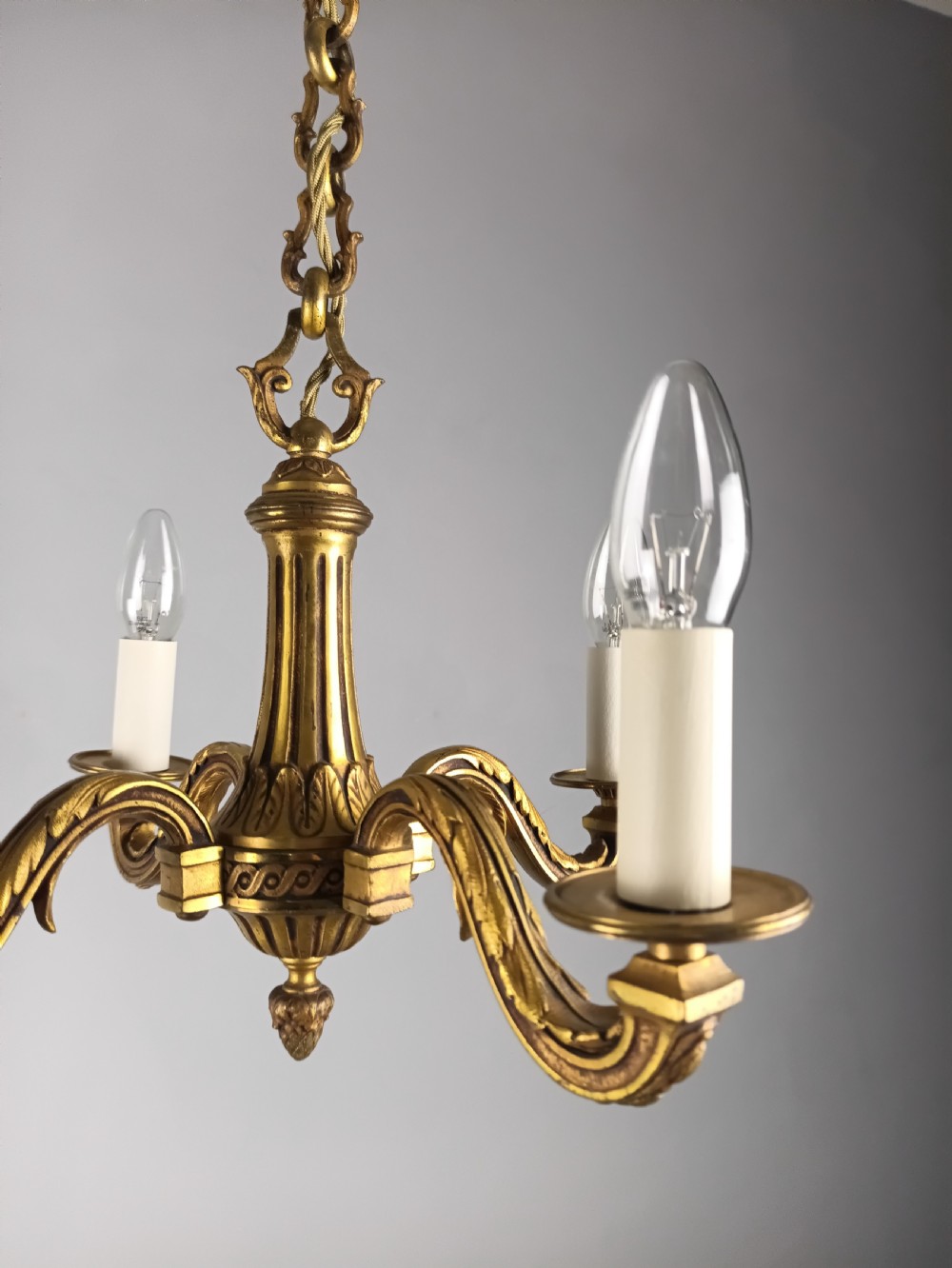 A French four-arm gilt bronze chandelier featuring acanthus leaf castings, white candle sleeves, and a suspended central chain. View XIV
