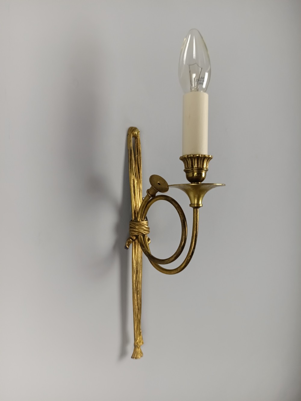 A single-arm French antique Louis XVI style wall sconce crafted from gilded brass with a horn motif arm and a white candle sleeve. View II