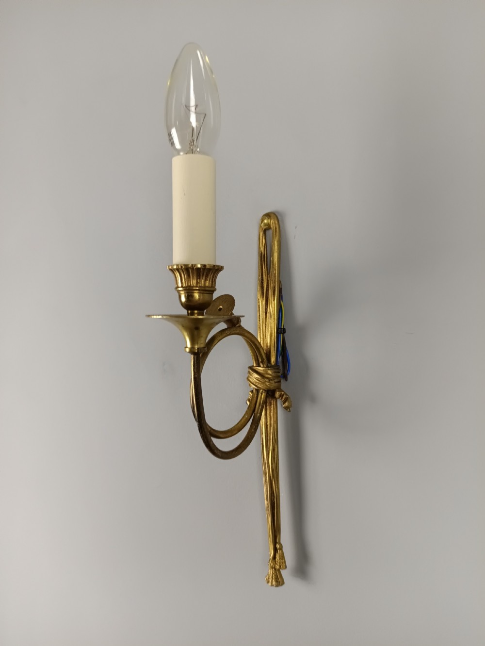 A single-arm French antique Louis XVI style wall sconce crafted from gilded brass with a horn motif arm and a white candle sleeve. View V