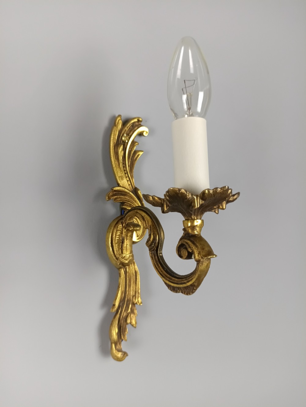 A pair of French Rococo style gilded bronze single-arm wall sconces featuring acanthus leaf scrollwork and candle-form sockets. View V