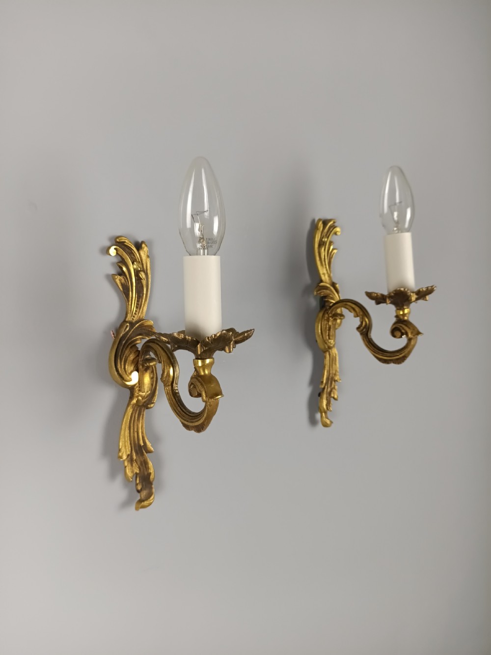 A pair of French Rococo style gilded bronze single-arm wall sconces featuring acanthus leaf scrollwork and candle-form sockets. View VIII