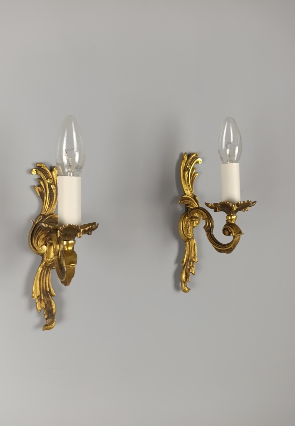 A pair of French Rococo style gilded bronze single-arm wall sconces featuring acanthus leaf scrollwork and candle-form sockets. View IX