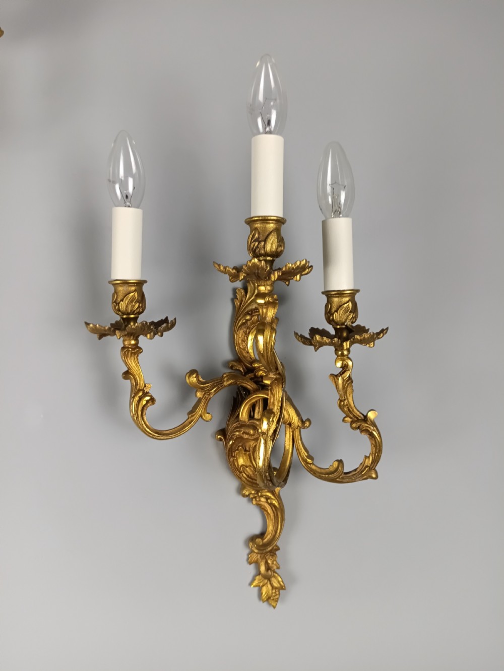 A pair of French Rococo style gilded bronze wall lights featuring three scrolling foliate arms and leaf motifs. View II
