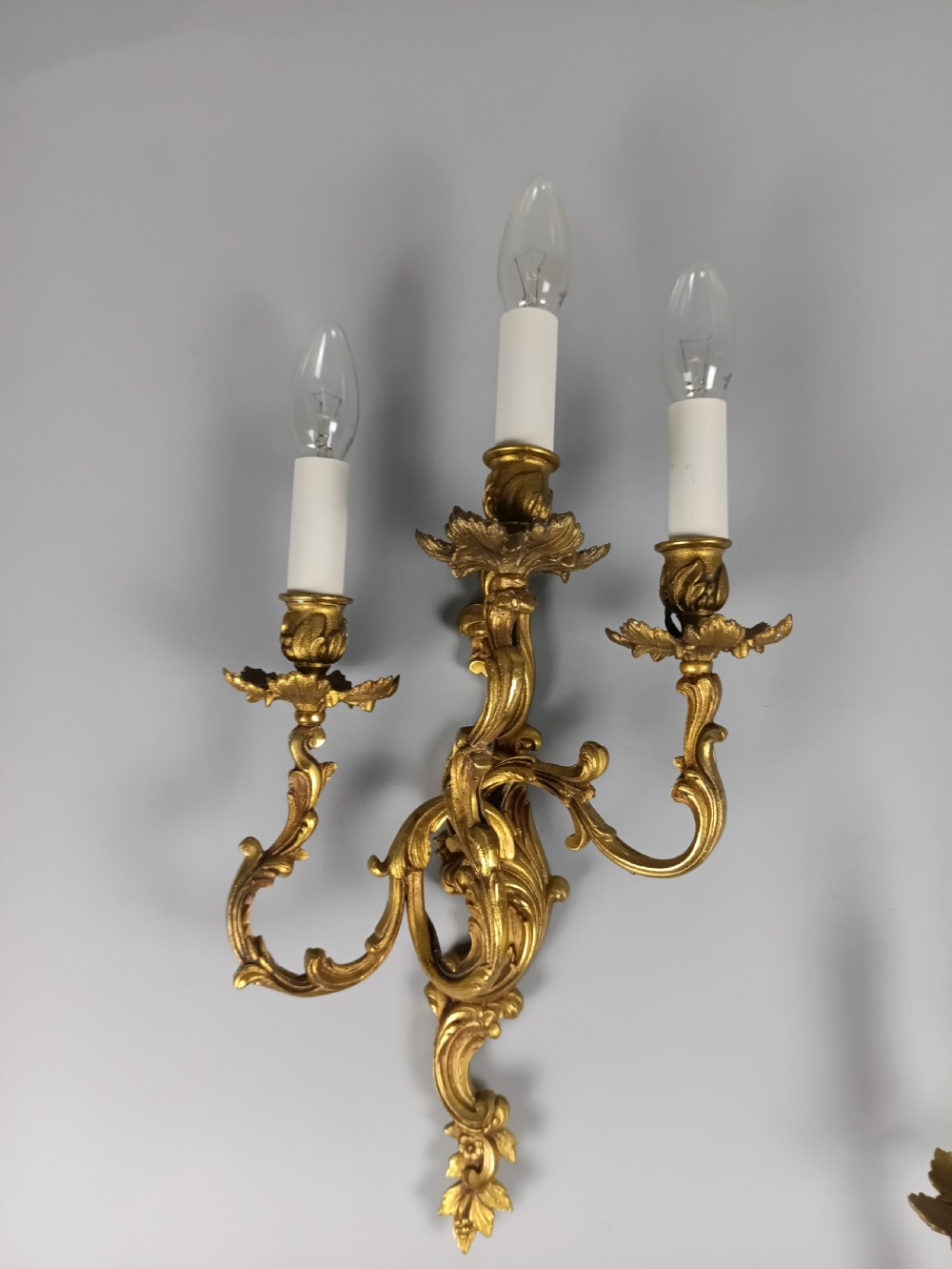 A pair of French Rococo style gilded bronze wall lights featuring three scrolling foliate arms and leaf motifs. View III