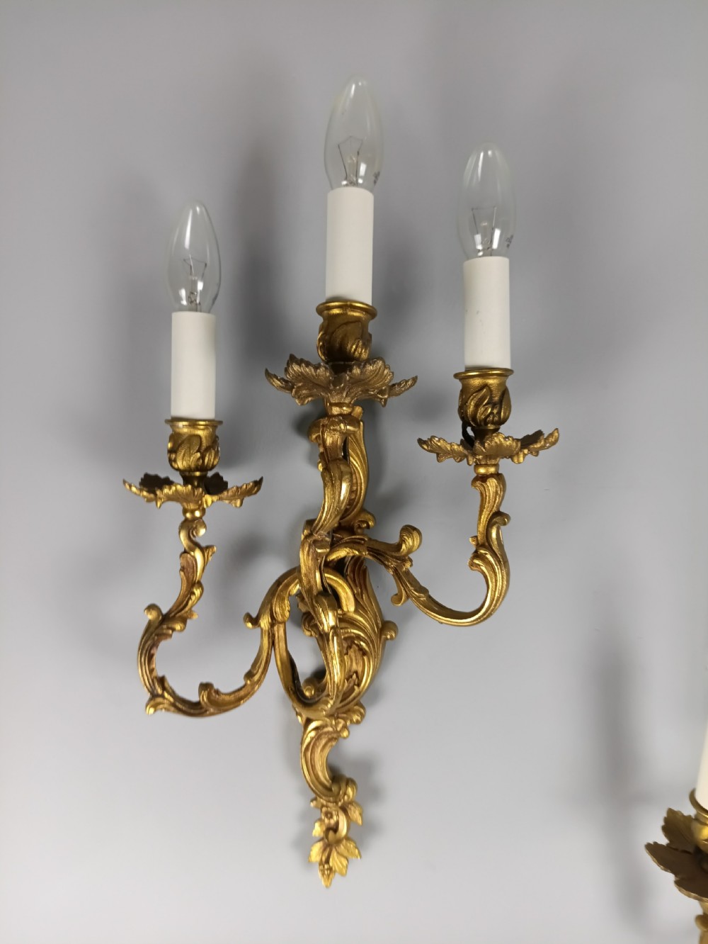 A pair of French Rococo style gilded bronze wall lights featuring three scrolling foliate arms and leaf motifs. View VII