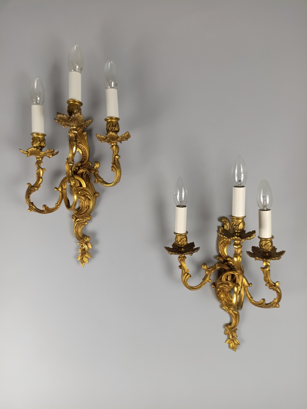A pair of French Rococo style gilded bronze wall lights featuring three scrolling foliate arms and leaf motifs. View VIII