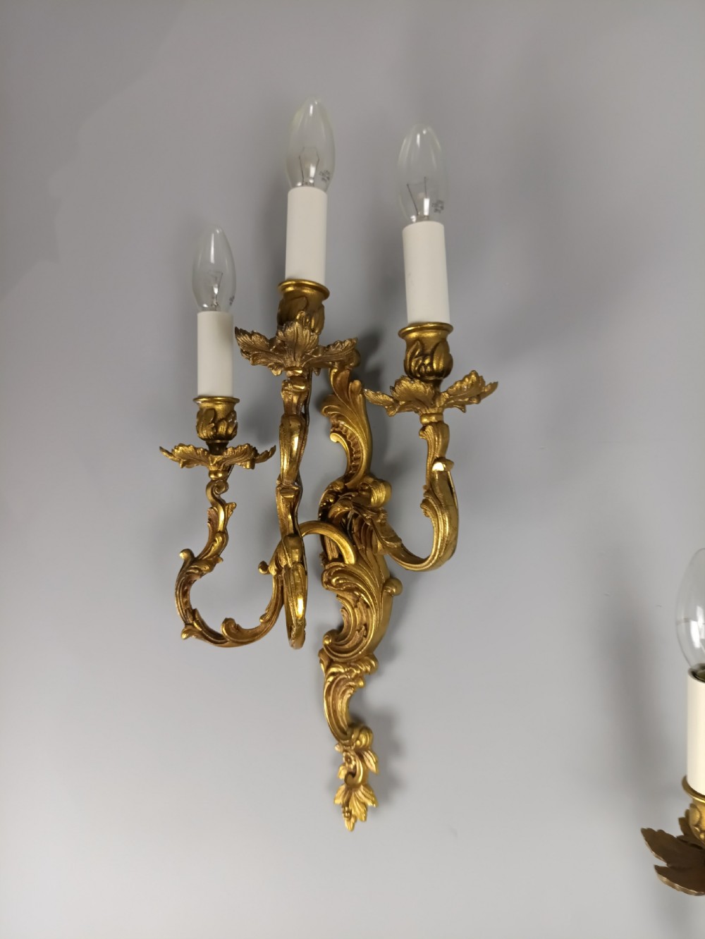 A pair of French Rococo style gilded bronze wall lights featuring three scrolling foliate arms and leaf motifs. View IX