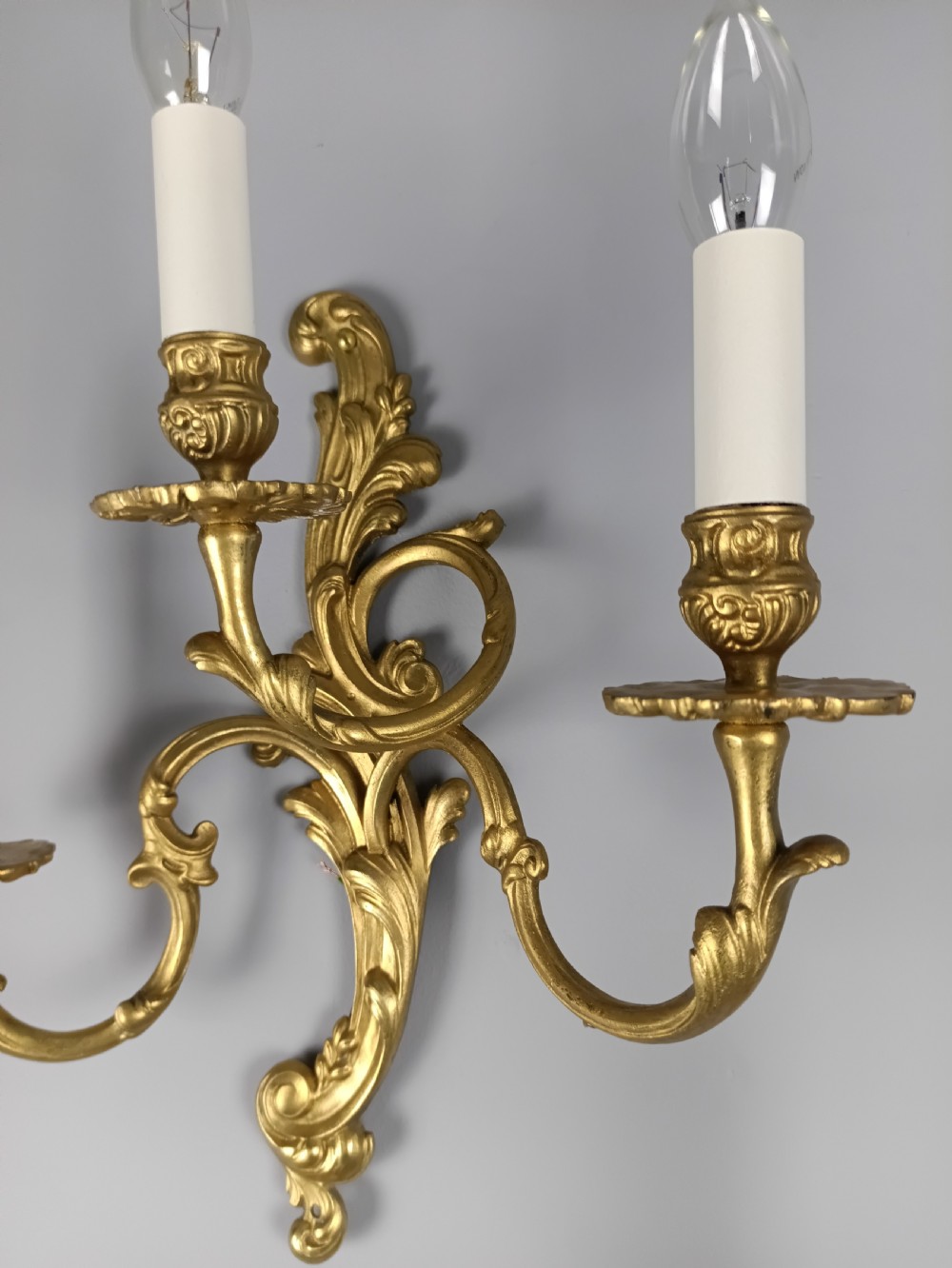 A pair of French Rococo style gilded brass triple arm wall sconces featuring ornate acanthus leaf scrollwork and candle shaped light fittings. View IV